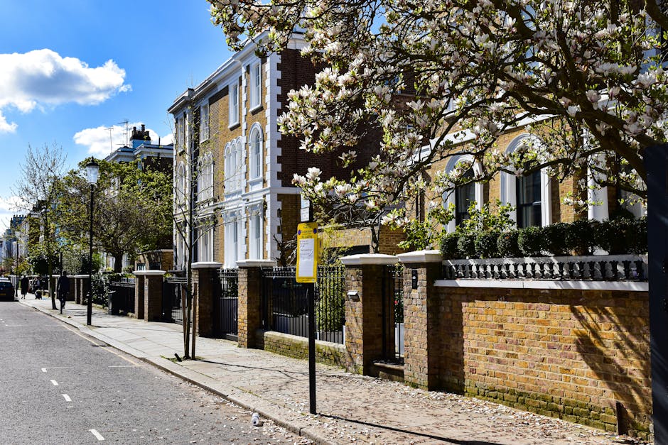 A row of Victorian-style terraced houses made of dark brick with white window frames and decorative stonework, situated along a paved street in a residential neighbourhood. The buildings have pitched 